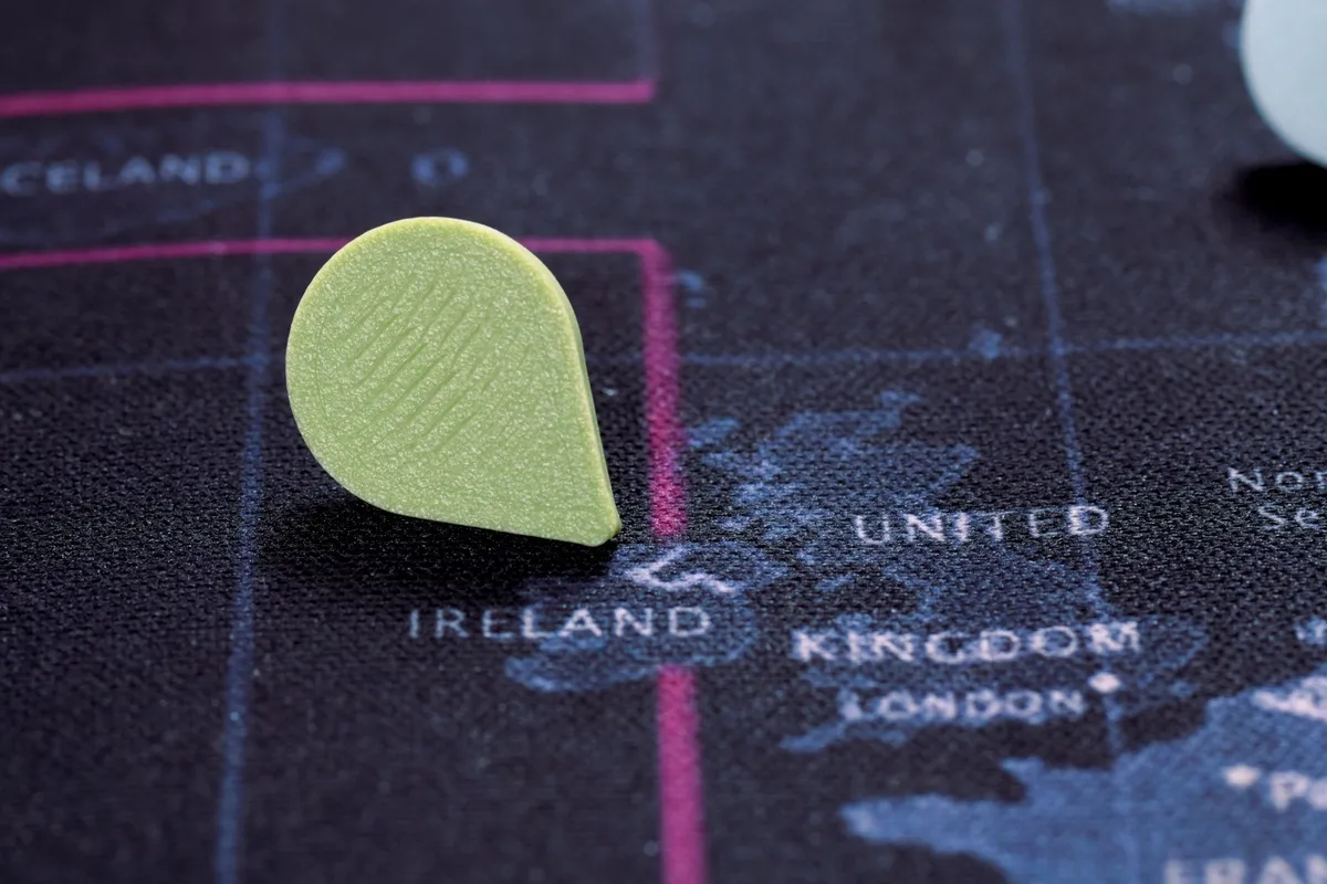Close-up of a green Touch-to-Travel pin pushed into a fabric map near Ireland and the United Kingdom