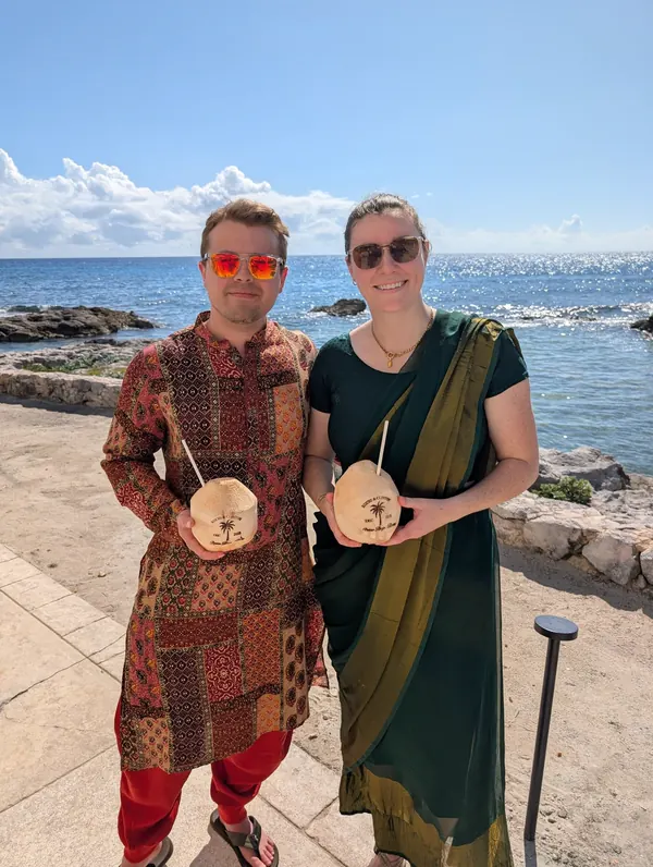 Hannah and Todd in Indian wedding clothes by the sea, holding coconuts